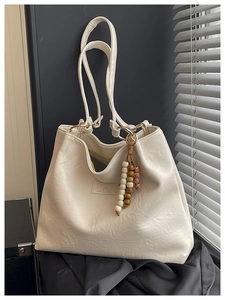 Detail of creamy white tote bag with textured faux leather and retro beaded tassel charm