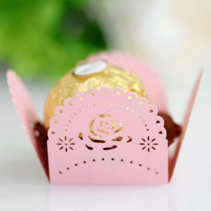 Macro view of laser-cut pink paper candy wrapper with rose heart patterns and gold chocolate