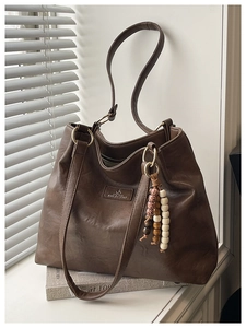 Close-up of deep brown tote bag with vintage bead charm and soft leather texture
