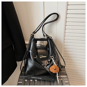 Détail d'un grand sac noir avec logo doré et ours en peluche posé sur une valise