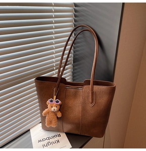 Detail of vintage brown leather tote bag with a cute bear charm by a window