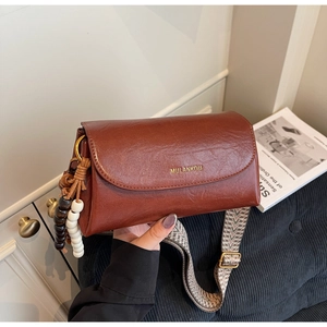 Detail of retro reddish brown PU leather bag with woven strap and bead pendant