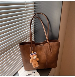 Detail of vintage brown leather tote bag with plush bear charm and zipper closure