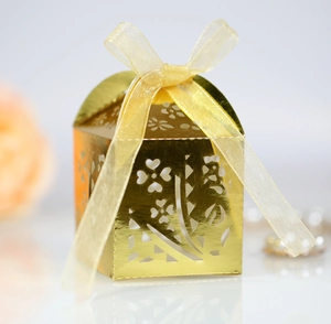Detail of laser-cut gold wedding favor box with floral heart patterns and silk ribbon