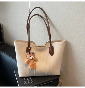 Detail of white tote bag with brown straps and cute plush bear charm on a book