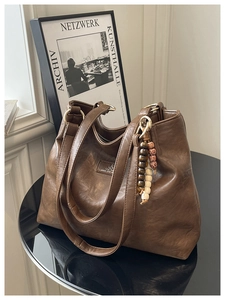 Close-up of vintage brown leather tote bag with gold ring hardware and beaded charm