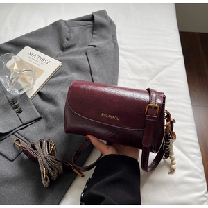 Detail of burgundy retro pillow bag with golden logo and vintage wood bead charm