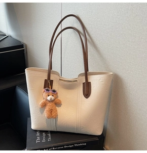 Detail of cream white tote bag with brown straps and cute teddy bear charm on books