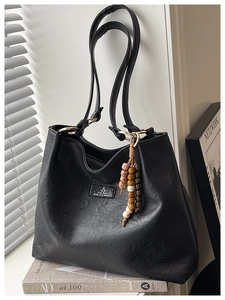Detail view of black vintage leather tote bag featuring golden hardware and beaded charm