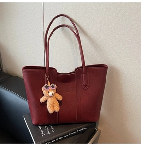 Detail of burgundy leather tote bag with stylish plush bear charm on books