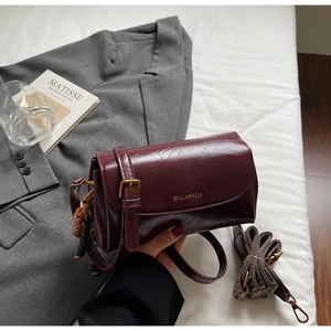 Detail of burgundy leather satchel with houndstooth strap and woven charm accessory