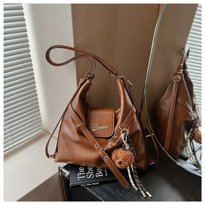 Détail du cabas en cuir marron foncé avec logo doré, charm ours et ruban décoratif