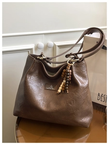 Close-up of brown vintage tote bag featuring wooden bead tassel and brand leather label