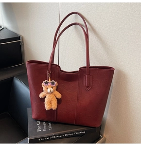 Detail view of burgundy tote bag with leather texture and cute plush bear charm