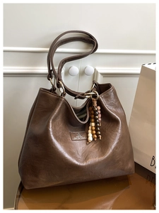 Detail view of deep brown vintage tote bag with ethnic bead charm on a wooden surface