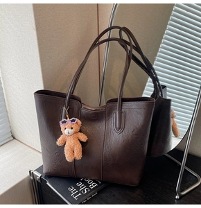 Detail of a large brown tote bag with leather texture and a plush bear pendant accessory
