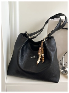 Detail of black pebbled leather tote bag featuring a brand label and beaded charm decoration