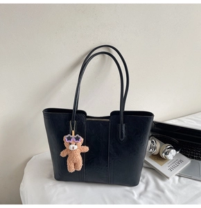 Detail of a black tote bag with a cute plush bear charm on a minimalist desk