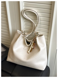 Macro detail of creamy white tote bag featuring vintage leather texture and wooden bead tassel