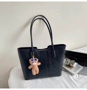 Detail of vintage black tote bag with leather texture and cute bear plush charm