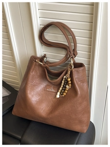 Detail of vintage brown leather tote bag showing wooden bead tassel and textured finish