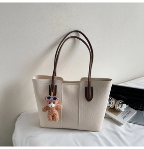 Detail of cream tote bag with wrinkled texture, brown straps and cute bear plush charm
