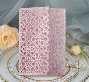 Close-up of pink glitter laser-cut lace invitation card with elegant pearl and rose decor