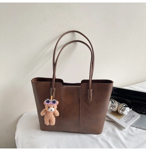 Detail of dark brown leather tote bag featuring a teddy bear charm and stylish setup