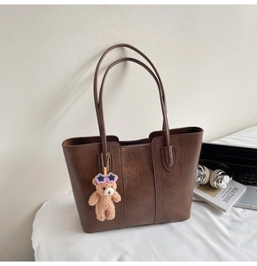 Detail of dark brown leather tote bag with plush bear charm and long shoulder straps