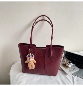 Detail of burgundy tote bag with faux leather texture and a cute brown bear charm