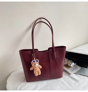 Detail of dark red tote bag with wrinkled texture and cute bear charm with sunglasses