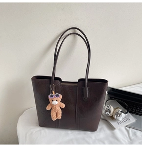 Detail of dark brown faux leather tote bag with vertical stitching and bear charm