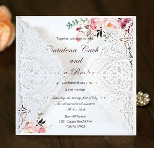 Detail of laser-cut lace wedding invitation with floral insert on dark wood table