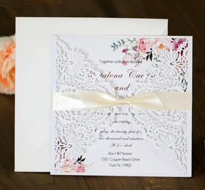 Detail of laser-cut wedding invitation with silk bow and floral liner on wooden background