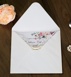 Detail of laser-cut lace wedding invitation with floral card on dark wood table
