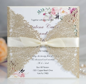 Detail of laser-cut gold glitter wedding invitation with elegant satin bow and floral insert