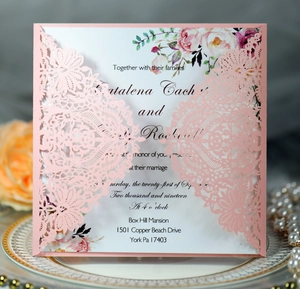 Detail of pink laser-cut wedding invitation with elegant floral insert on dinner plate