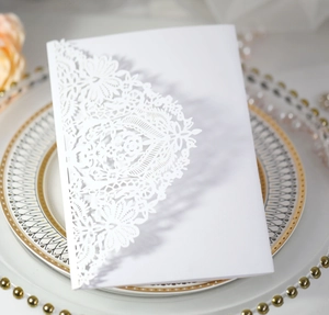 Detailed macro view of white laser-cut floral lace wedding invitation card on elegant plate