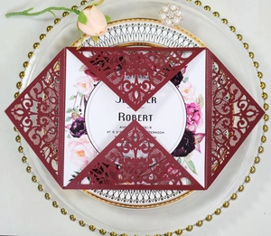 Macro view of burgundy laser-cut lace wedding invitation with floral printed inner card