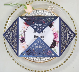 Navy blue laser-cut lace wedding invitation with floral insert on a decorative plate