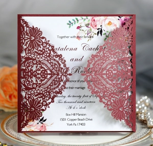 Macro shot of burgundy laser-cut wedding invitation with lace patterns and floral inner card