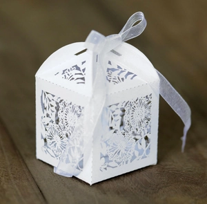 Detail of laser-cut wedding favor box with floral patterns and a purple ribbon bow