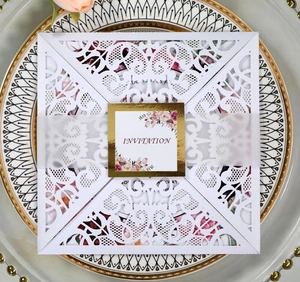 Intricate laser-cut square wedding invitation with elegant gold-foiled floral label