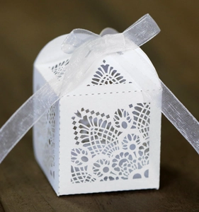 Close-up of laser cut ivory favor box with intricate floral pattern and white ribbon