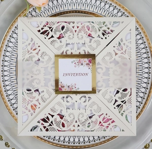 Macro detail of laser cut wedding invitation set with floral tag on a gold ceramic plate