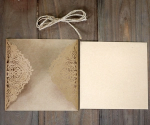 Detail of laser-cut floral kraft paper wedding invitation with jute twine on wood