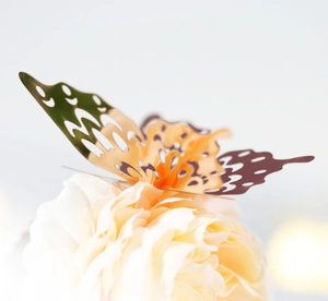 Close-up of golden 3D hollow butterfly decor with geometric patterns on a soft flower