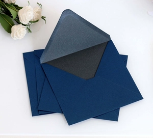 Macro view of pearlescent deep blue wedding envelopes with elegant white rose decor