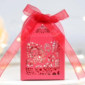 Detailed view of red laser-cut wedding favor box with elegant floral pattern and silk ribbon