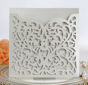 Detail of laser-cut silver wedding invitation with intricate heart vine pattern on a plate